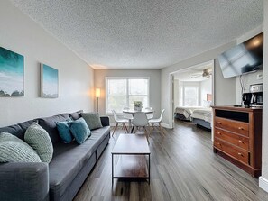 A modern living room with a sofa, coffee table, and a TV. There is a dining area with a table and chairs. - Disney Condo With Resort Pool Sleeps 6 (Kissimmee)