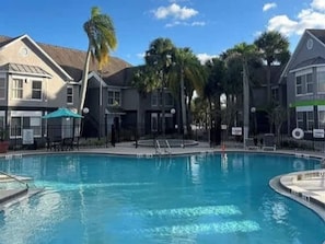 A swimming pool surrounded by buildings with a clear sky. - Disney Condo With Resort Pool Sleeps 6 (Kissimmee)