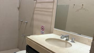A bathroom with a toilet, sink, mirror, and shower.