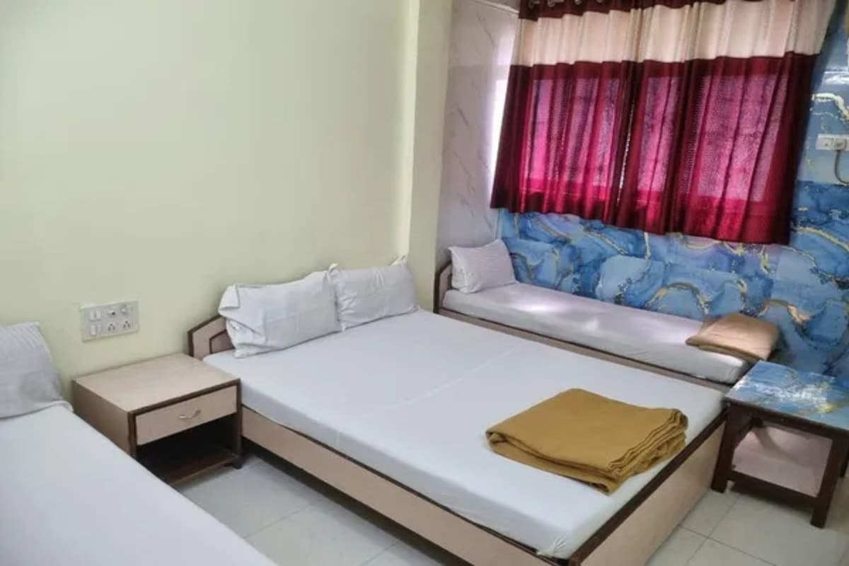 A single-bed room with a bedside table, a window with curtains, and a patterned wall.