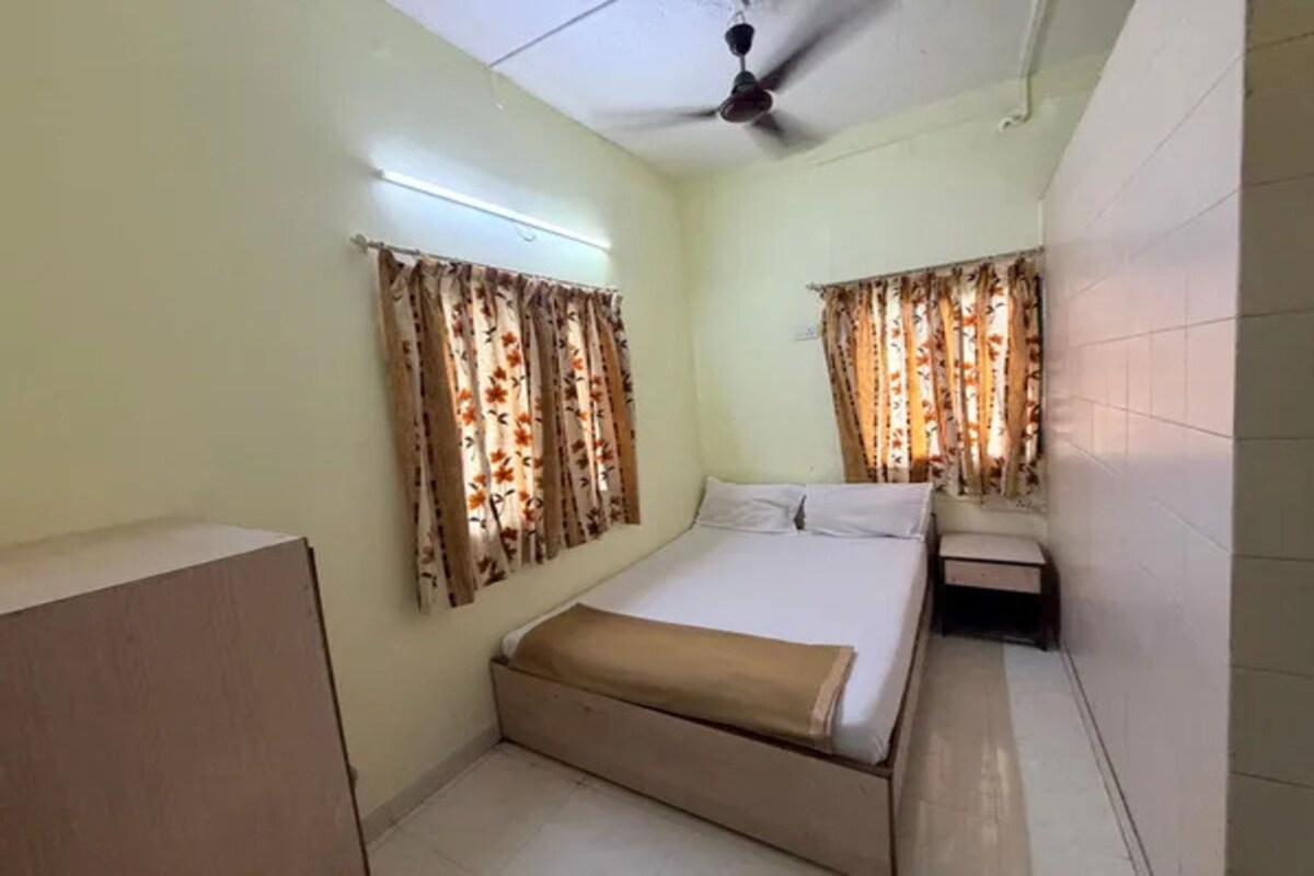 A room with a bed, a bedside table, a ceiling fan, and curtains.