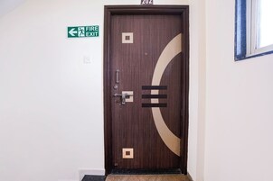 Una puerta con un cartel de salida de emergencia encima, el número '202' en la pared y una ventana a la derecha.