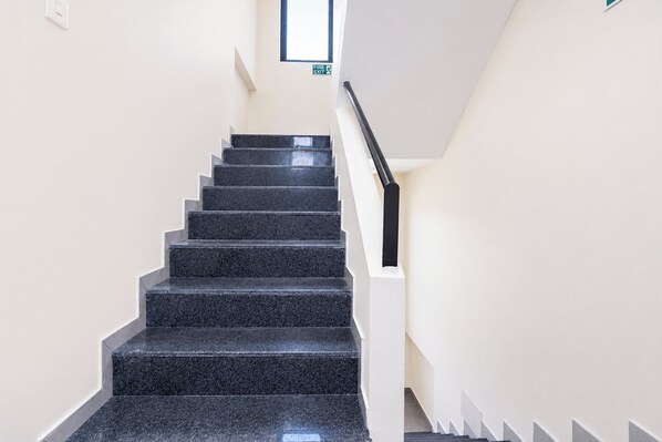 A staircase with black steps and white walls, leading to an exit sign above.