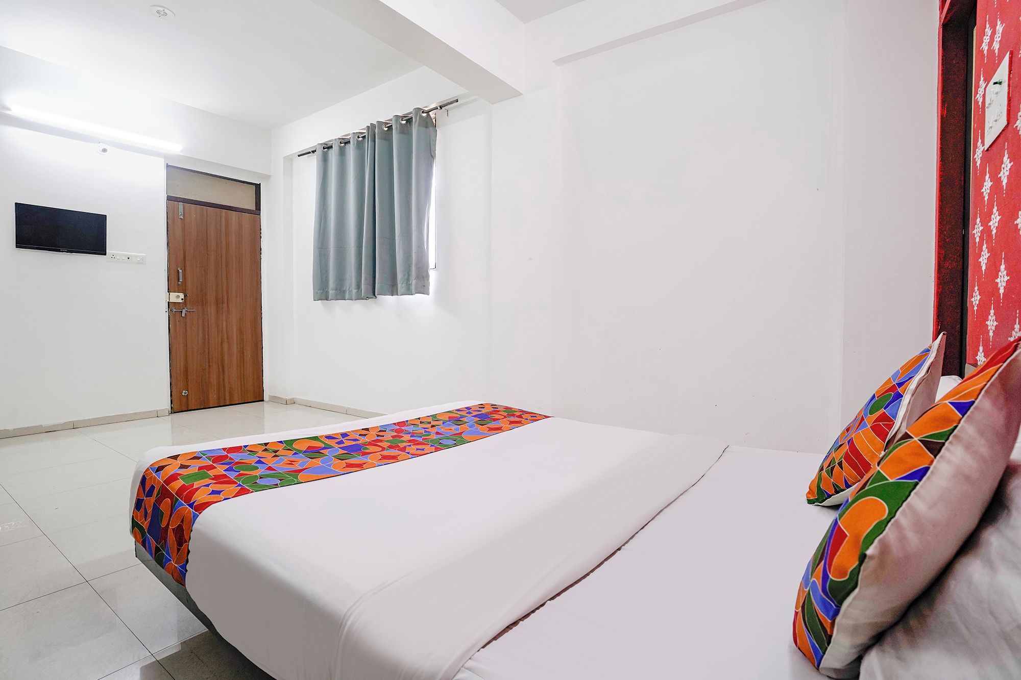 Quarto de hotel com cama, televisão, porta e janela com cortinas.