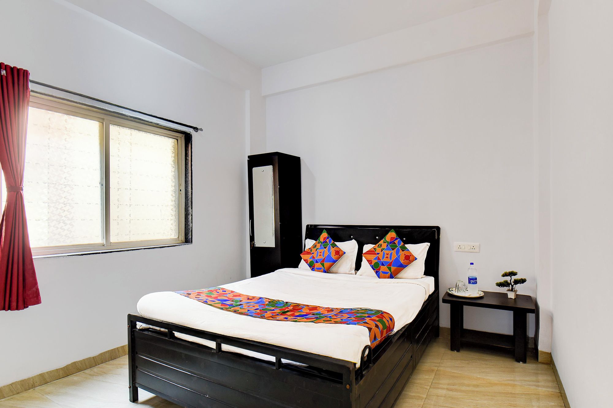 A bedroom with a bed, a nightstand, a mirror, and a window with curtains.