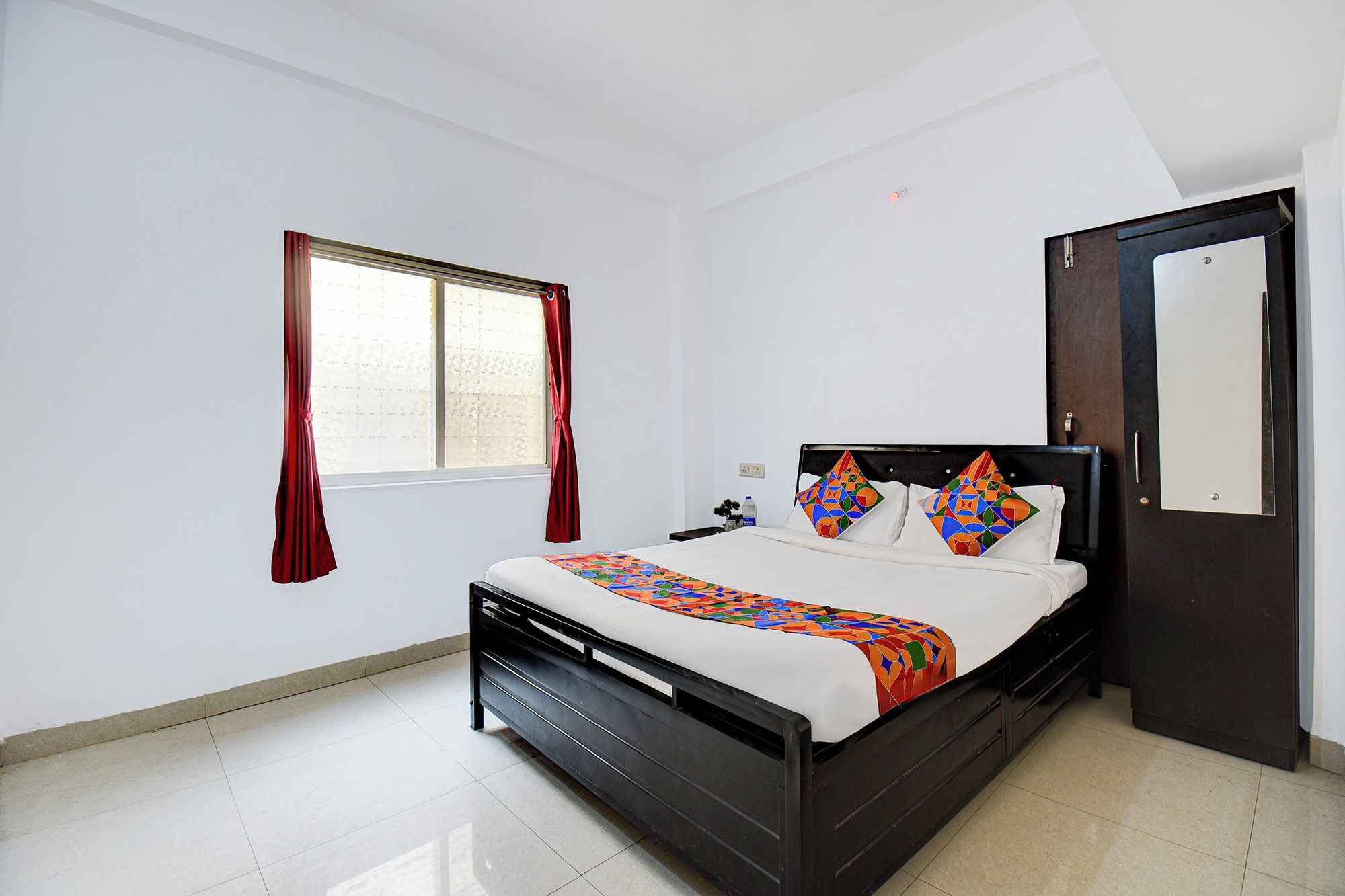 Un dormitorio con cama, ventana con cortinas, mesita de noche y puerta.