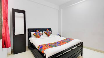 Una cama bien hecha con una colcha y almohadas de estampado geométrico colorido, un cabecero negro y una pared blanca.