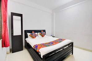 A neatly made bed with a colorful geometric-patterned bedspread and pillows, a black headboard, and a white wall.