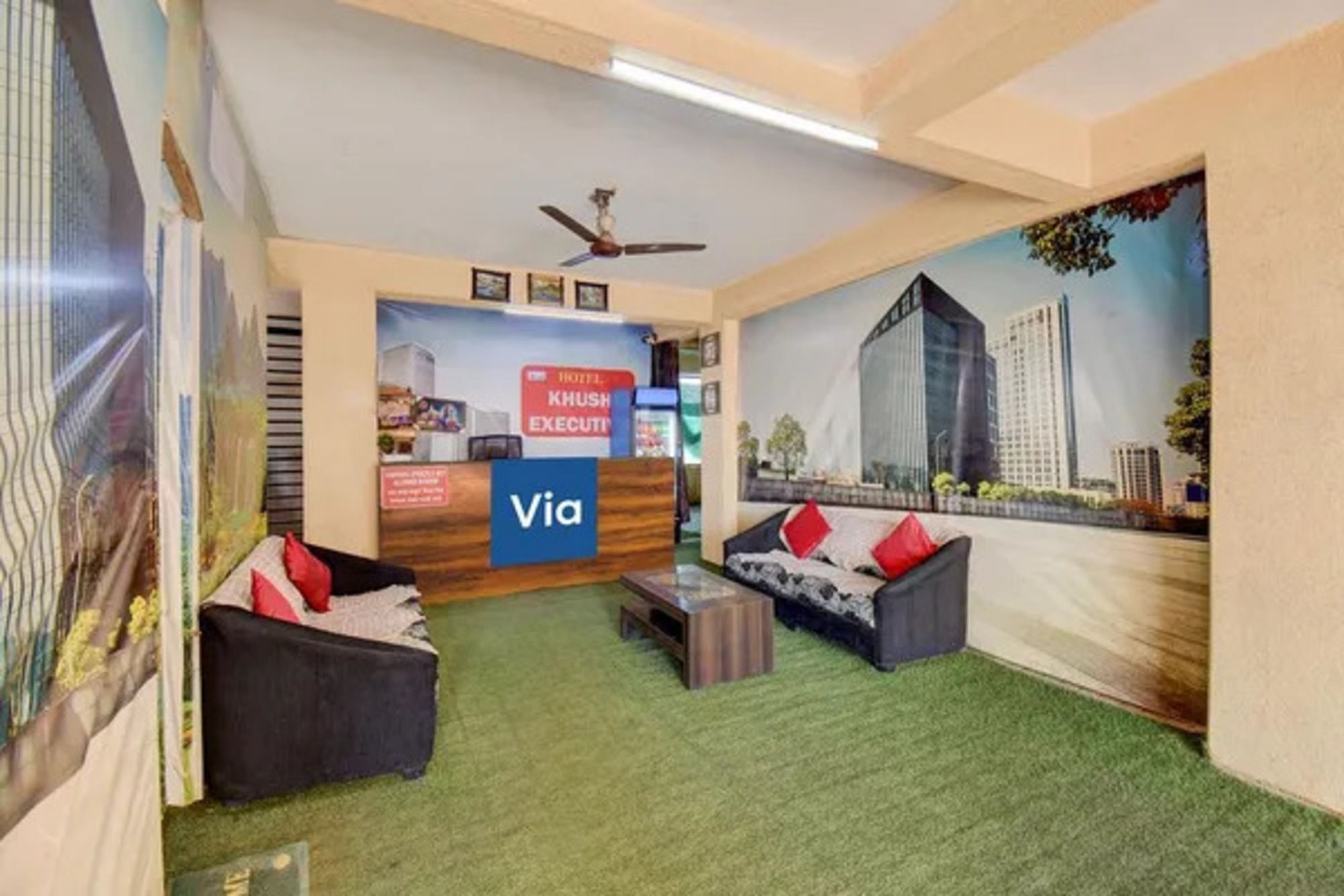 A hotel lobby with a reception desk, a ceiling fan, and a mural of buildings.