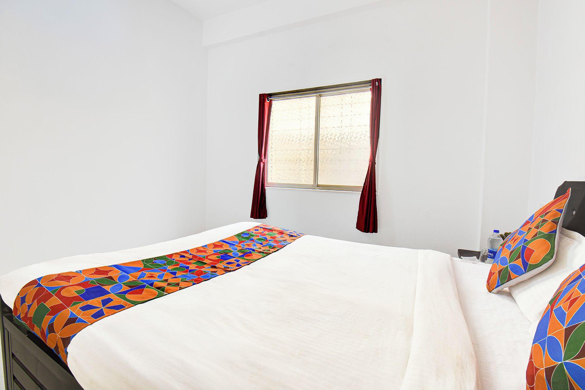 Una habitación de hotel con una cama, una ventana con cortinas y una almohada con un estampado geométrico de colores.