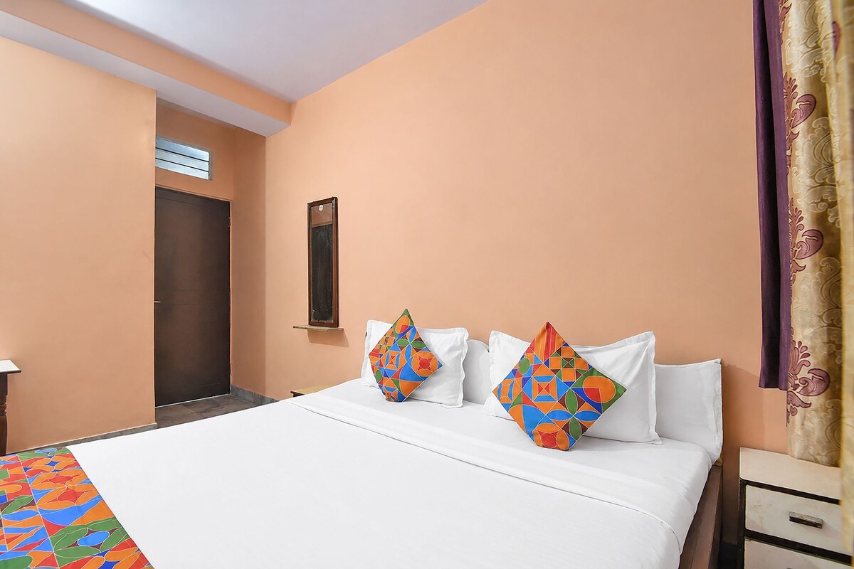 Una habitación de hotel con una cama, dos almohadas con diseños geométricos, una mesita de noche, un espejo y una puerta.