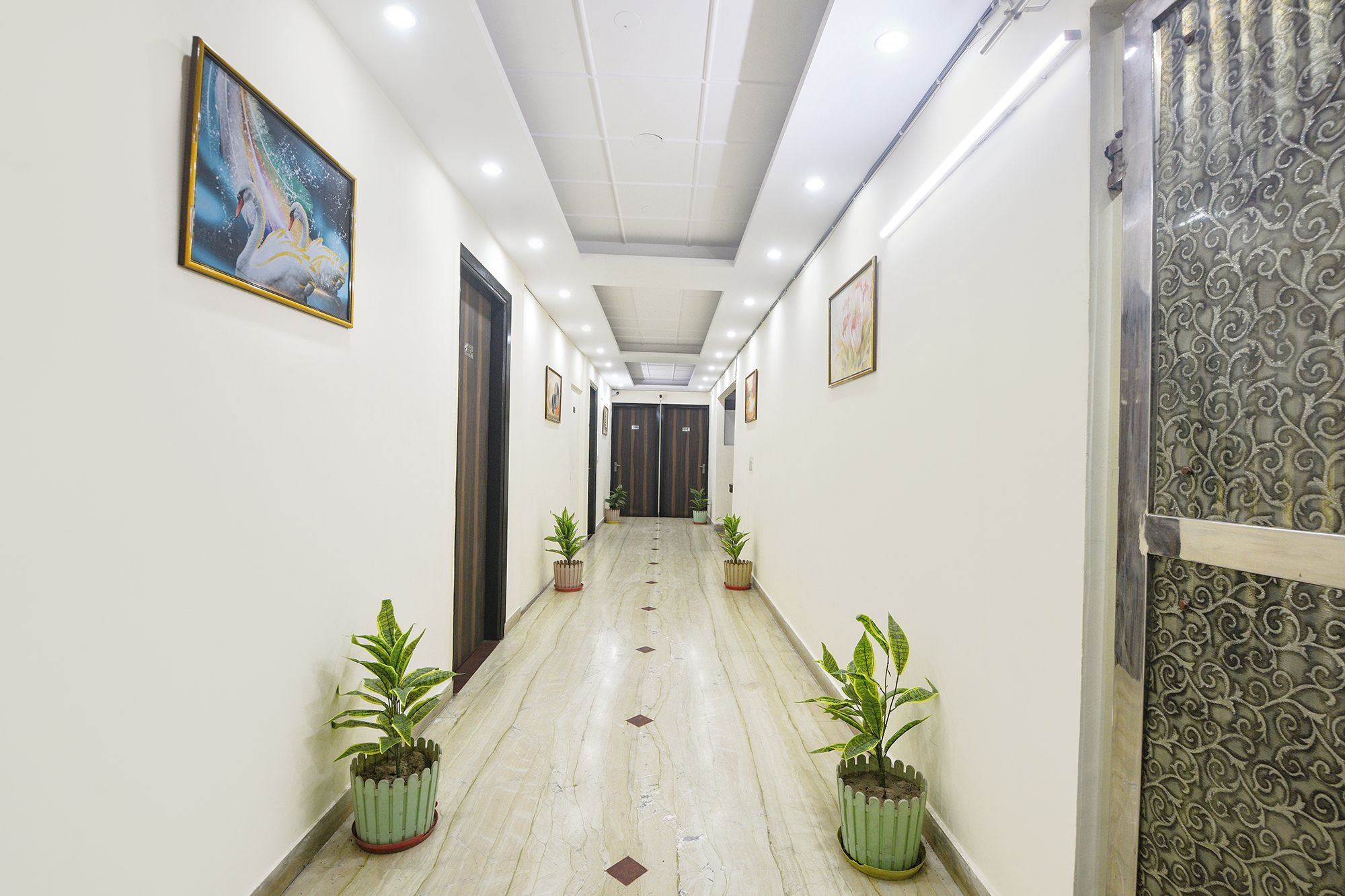 A hallway with a marble floor, potted plants, framed artwork, and a patterned wall.
