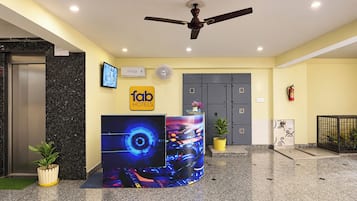 Ein Hotel-Empfangsbereich mit modernem Design, inklusive eines digitalen Displays, einem Deckenventilator und einer Rezeption.