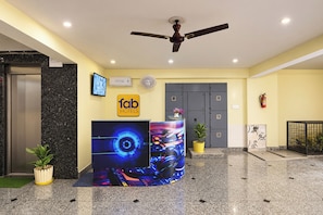 Uma área de recepção de hotel com design moderno, incluindo um painel digital, um ventilador de teto e um balcão de atendimento.