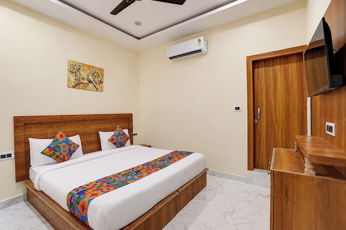 Habitación de hotel con cama de madera, ventilador de techo, equipo de aire acondicionado, televisor y armario de madera.