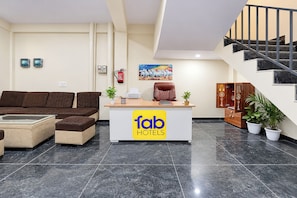 Zona de recepción de un hotel con un sofá, un escritorio, un extintor y una escalera.