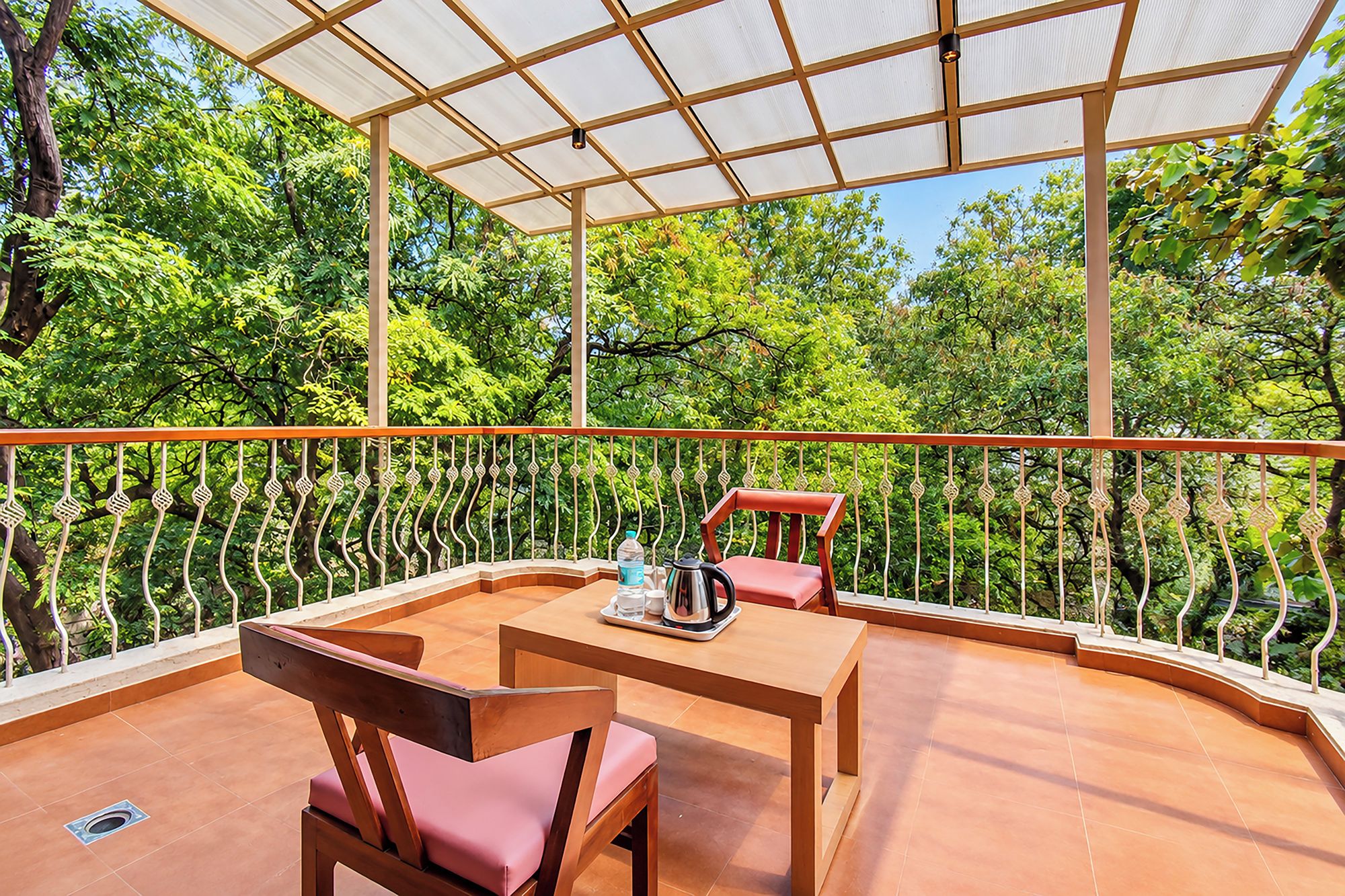 Terraço ao ar livre com mesa e cadeiras, rodeado por um guarda-corpo de metal e vista para vegetação exuberante.