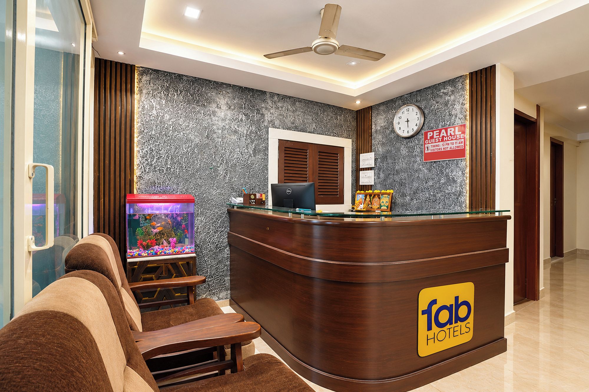 A hotel reception area with a wooden reception desk, a clock, a fish tank, and a sign indicating guest hours.
