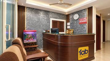 A hotel reception area with a wooden reception desk, a clock, a fish tank, and a sign indicating guest hours.