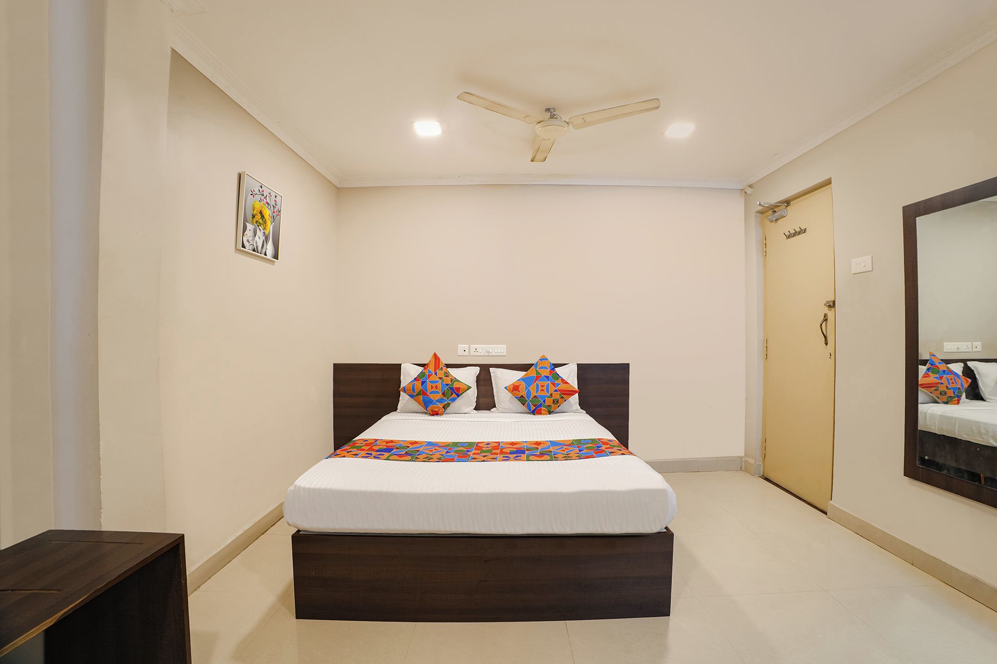 A hotel room with a bed, a ceiling fan, a door, and a mirror.