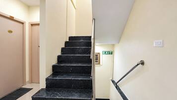 A staircase with a handrail leading to an exit, a door with a number plate, and a wall-mounted light switch.