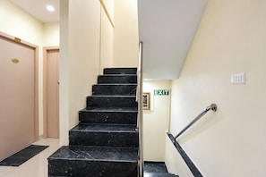Gradi amb barana que condueix a una sortida, una porta amb una placa amb número, i un interruptor de llum fixat a la paret.
