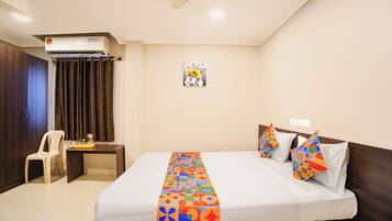 A hotel room with a bed, a desk, a chair, an air conditioning unit, and a wall-mounted picture.