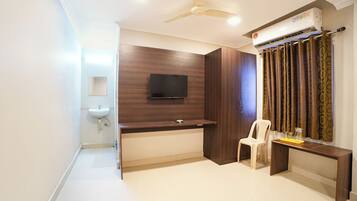 A room with a flat-screen TV mounted on a wooden wall, a ceiling fan, an air conditioning unit, a white sink, and a small table with a chair.