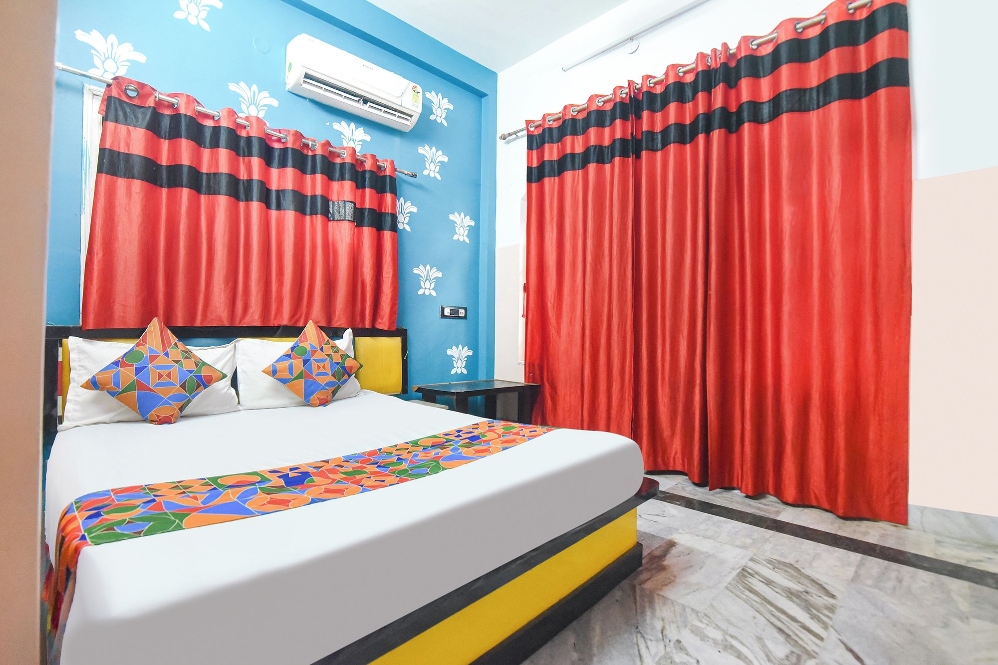 Habitación de hotel con cama, mesita de noche, aire acondicionado instalado en la pared y cortinas rojas.