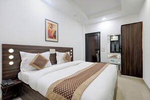 A hotel room with a bed, bedside table, lamp, and a painting on the wall. - FabHotel Jpm Hd Home Stays (New Delhi)