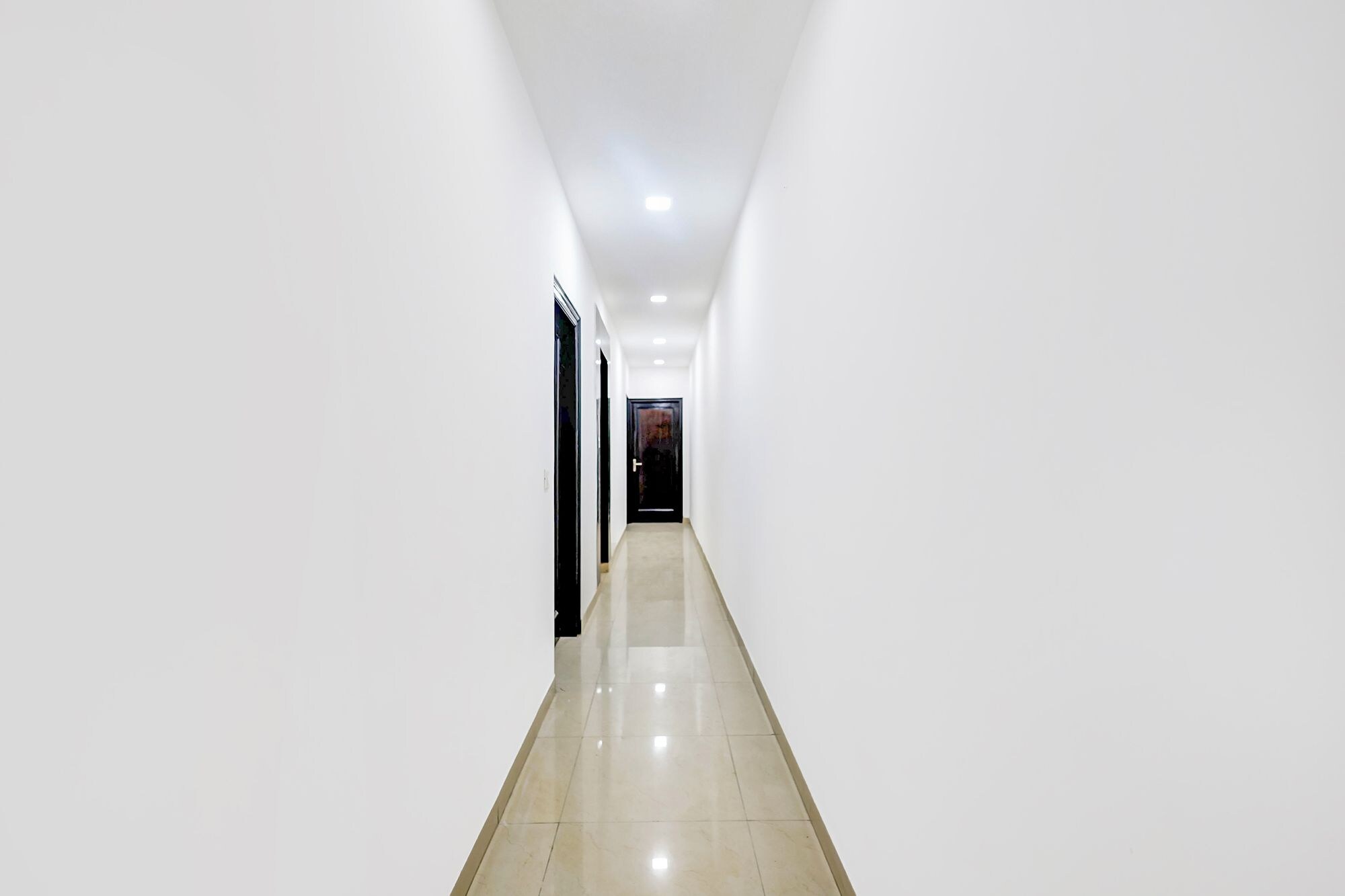 A long, narrow hallway with white walls and a shiny floor, leading to a door at the end.