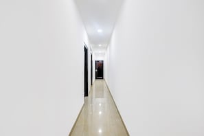 A long, narrow hallway with white walls and a shiny floor, leading to a door at the end. - FabHotel Jpm Hd Home Stays (New Delhi)