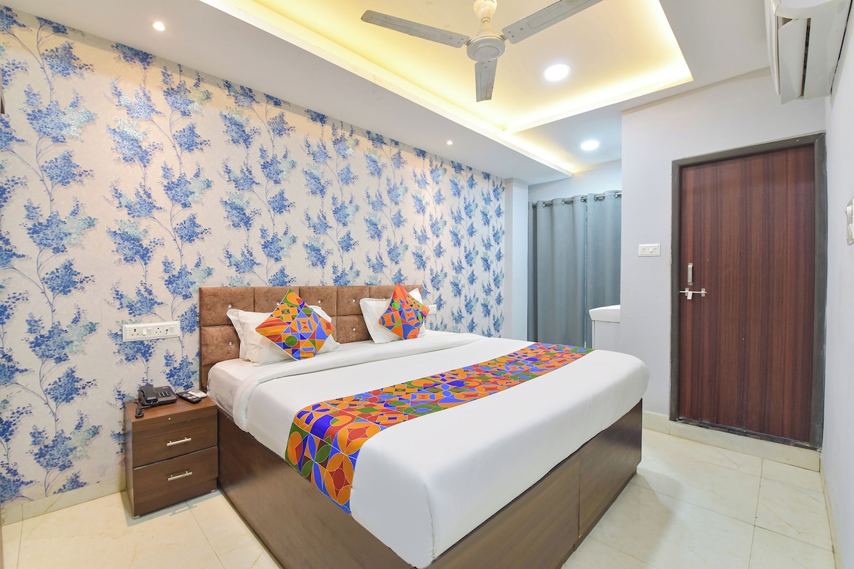 A hotel room with a bed, a nightstand, a wooden wardrobe, a ceiling fan, and a bathroom with a curtain.