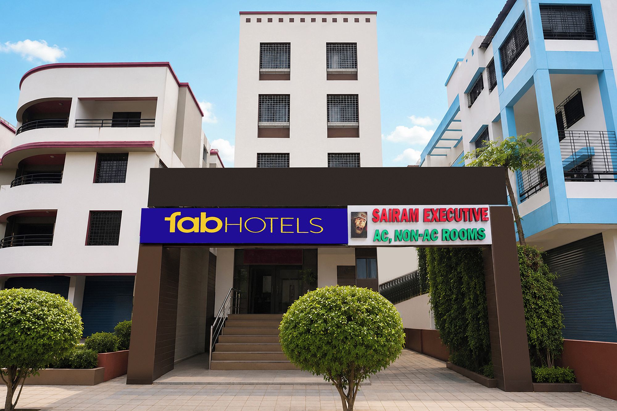 Entrada de hotel com placa indicando 'fabHOTELS' e 'QUARTOS EXECUTIVOS SAIRAM, SEM AR CONDICIONADO'.
