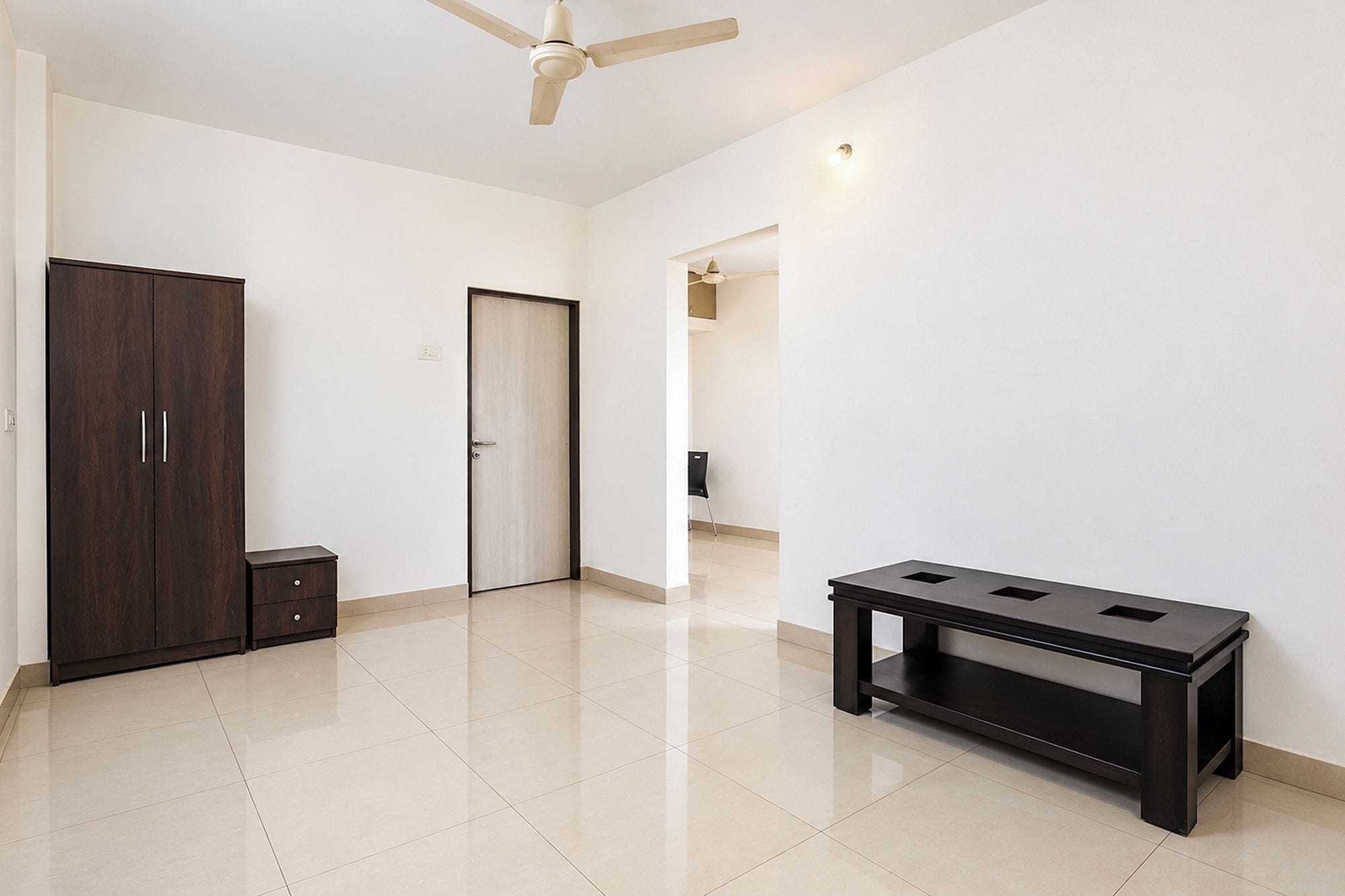 A room with a ceiling fan, a wardrobe, a door, and a small table.