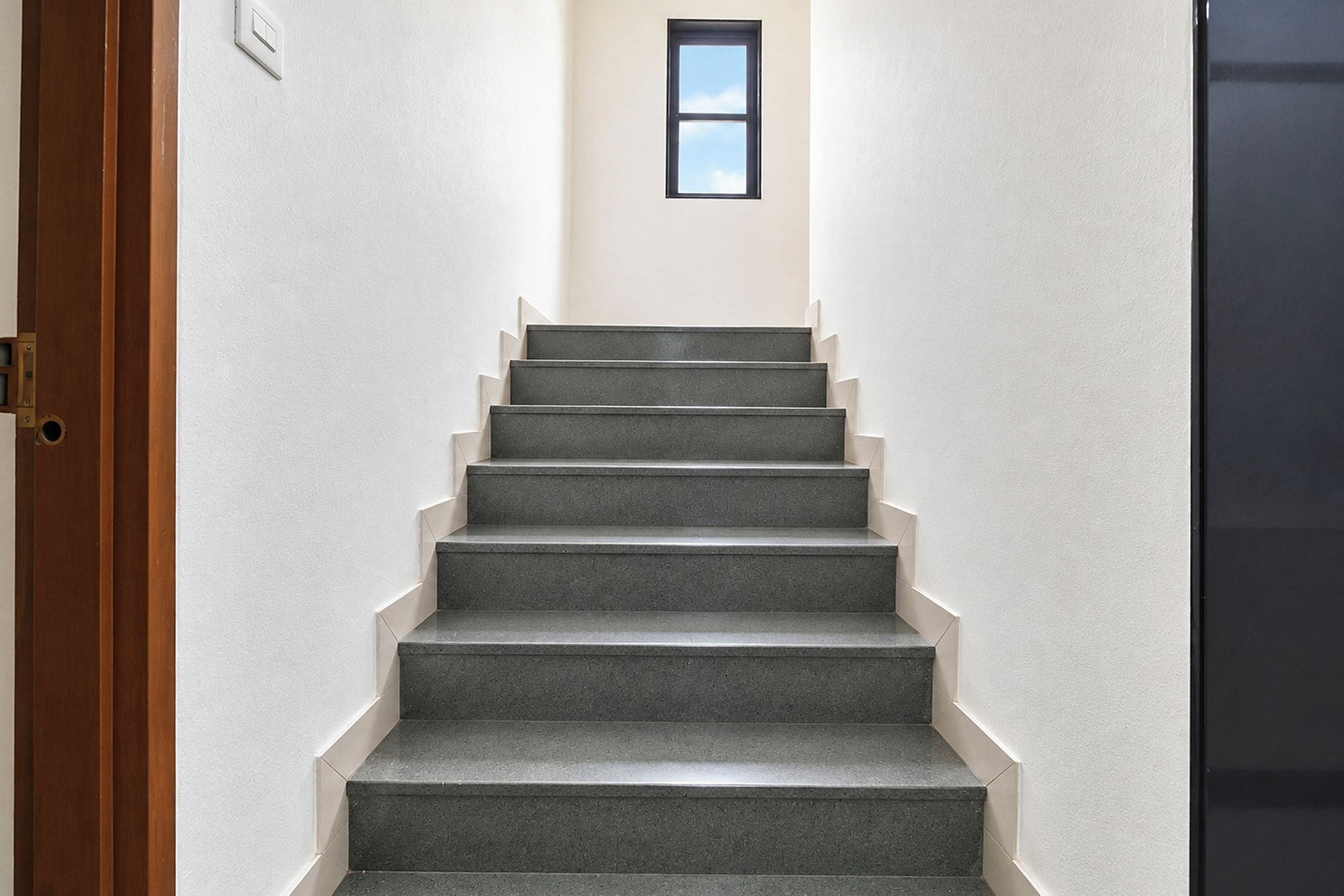 Una escalera con barandilla que lleva a un rellano con un ventanal pequeño.