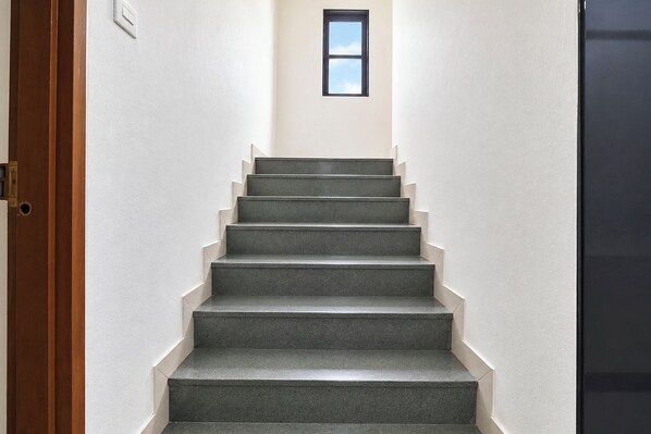 A staircase with a handrail, leading to a landing with a small window. - FabHotel Sairam Executive (Pune)