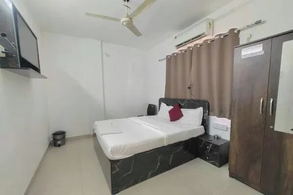 A bedroom with a bed, a wardrobe, a ceiling fan, and a small bedside table. - FabHotel Sairam Executive (Pune)