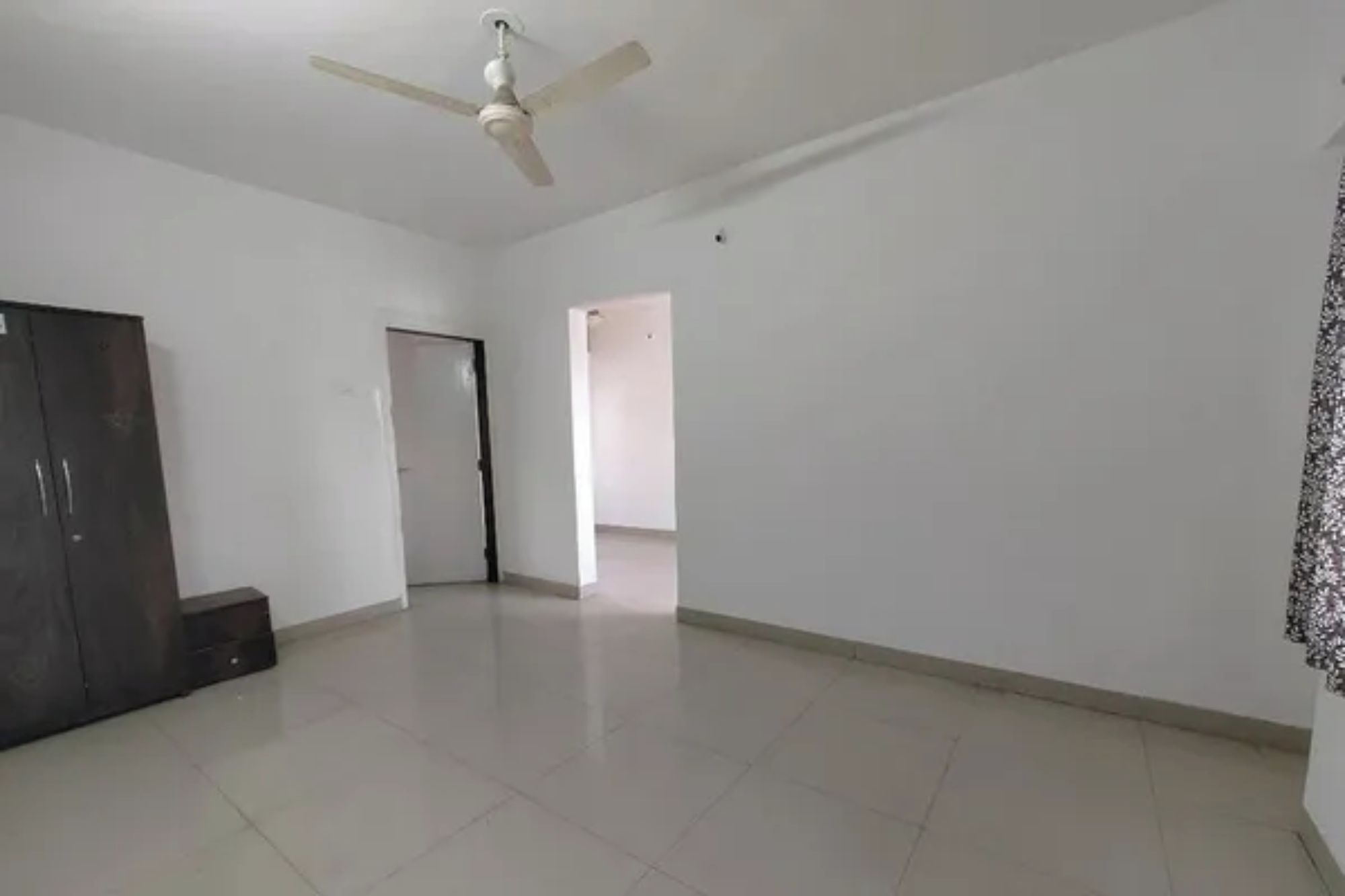 Una habitación amplia con ventilador de techo, un armario y una puerta que da a otra habitación.