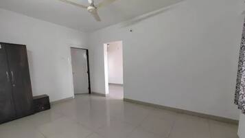 A spacious room with a ceiling fan, a wardrobe, and a door leading to another room.