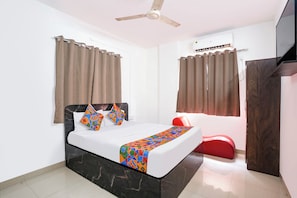 A modern hotel room with a bed, curtains, a ceiling fan, an air conditioning unit, and a red chair. - FabHotel Sairam Executive (Pune)