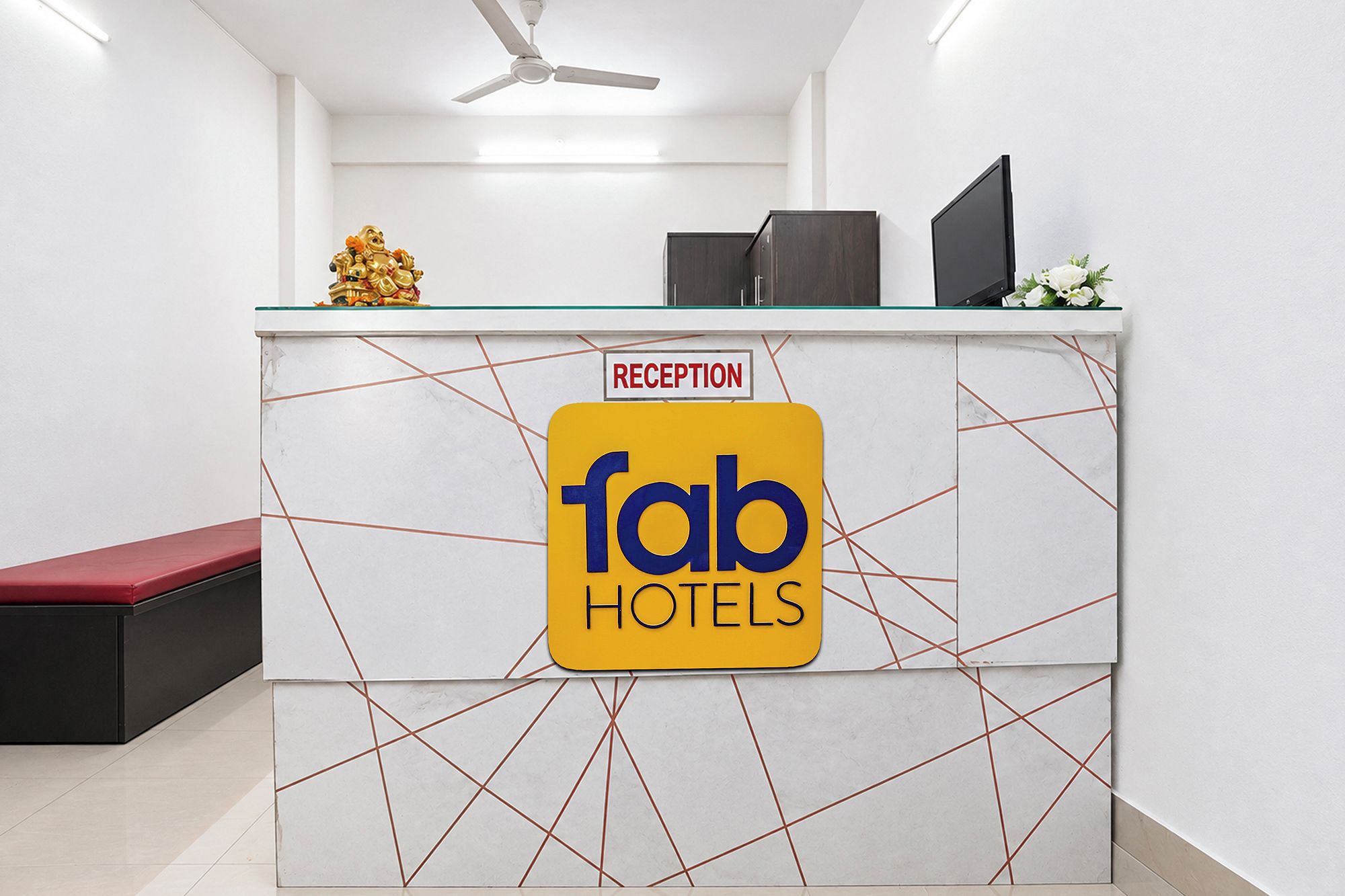 Una recepción con un cartel de 'fab hotels', un área de recepción y un banco rojo.