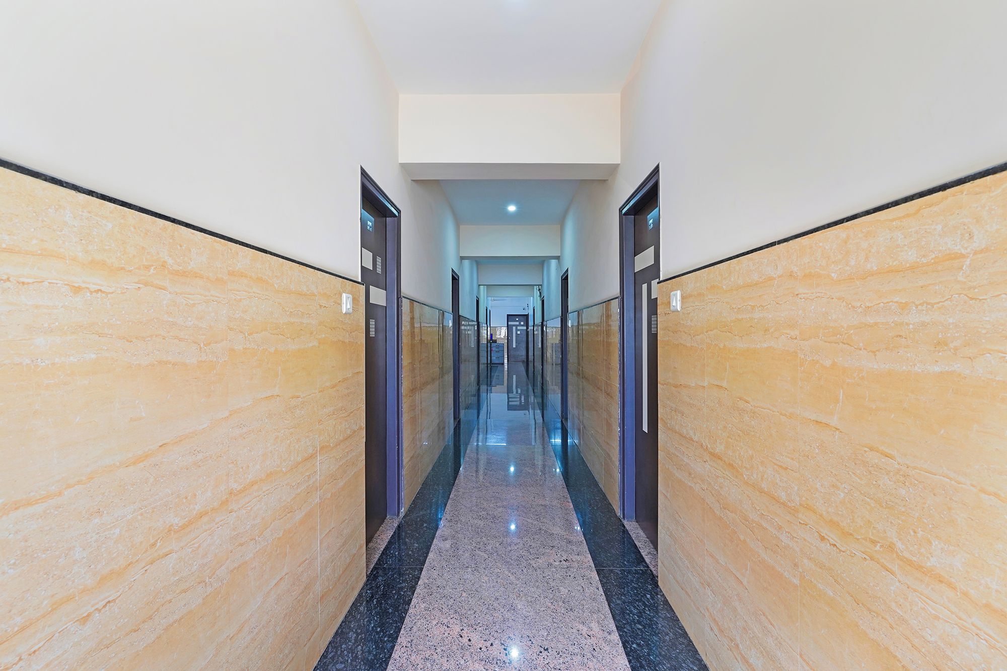 A long, narrow hallway with marble walls and a polished floor, leading to a door at the end.