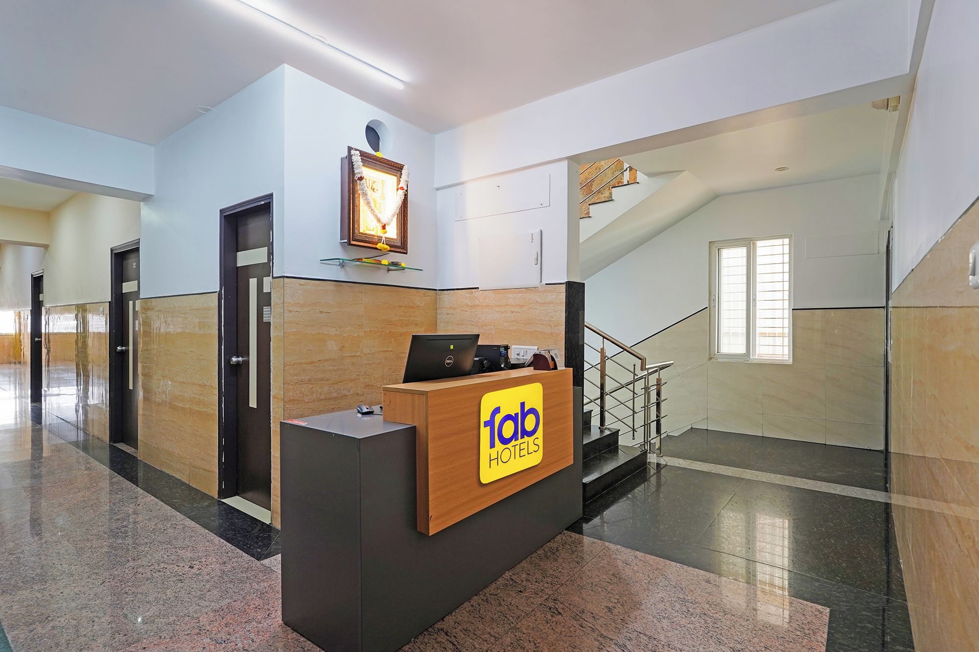 Zona de recepción de hotel con un mostrador, una escalera y una lámpara fijada a la pared.