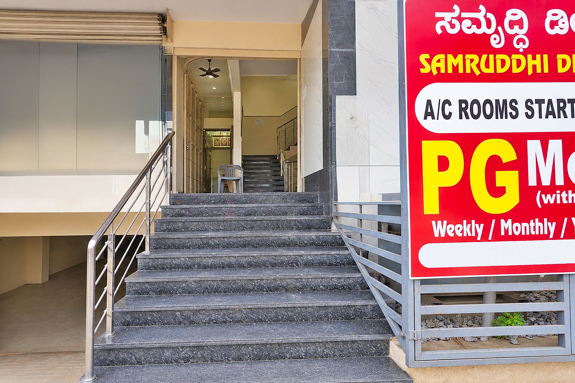 A staircase leading to a building entrance with a sign advertising A/C rooms starting at PG 1500.