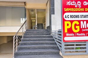 Una escalera conduce a la entrada de un edificio, con un cartel que anuncia habitaciones con aire acondicionado desde PG 1500.