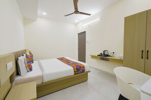 A hotel room with a bed, a desk, a chair, a wardrobe, and a ceiling fan.