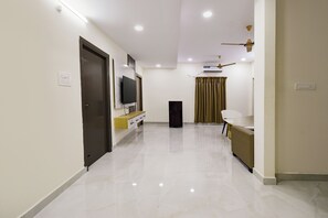 A hallway with a flat-screen TV mounted on the wall, a small cabinet, a black speaker, and a ceiling fan.