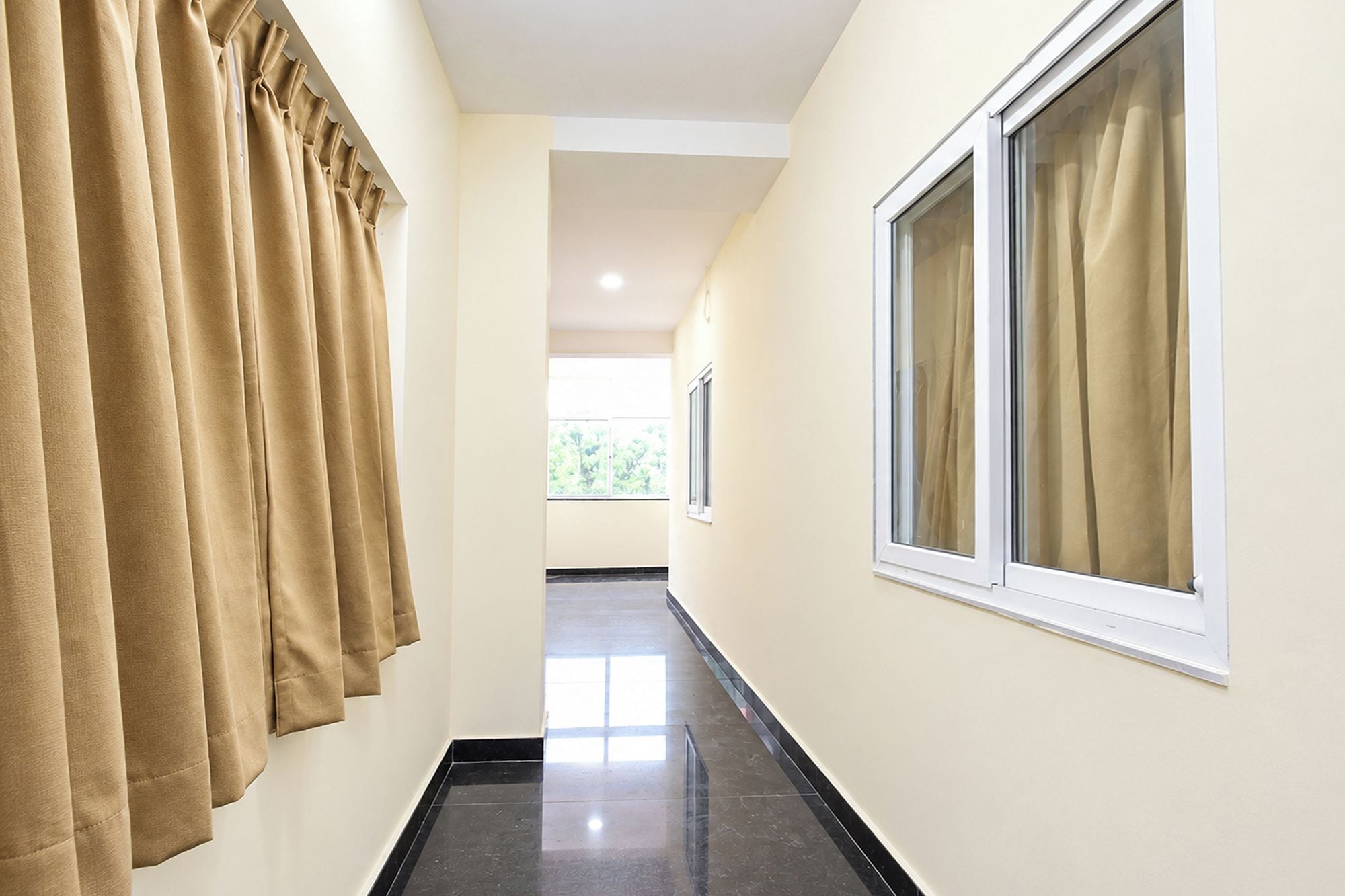Un pasillo con cortinas color beige, una ventana y piso de baldosas.