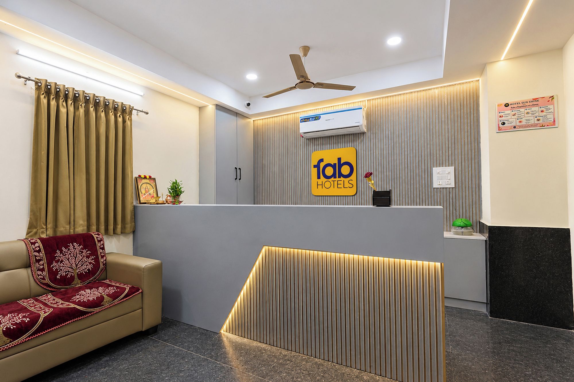 Un área de recepción de hotel con diseño moderno, que incluye un mostrador de recepción, un ventilador de techo y un equipo de aire acondicionado mural.